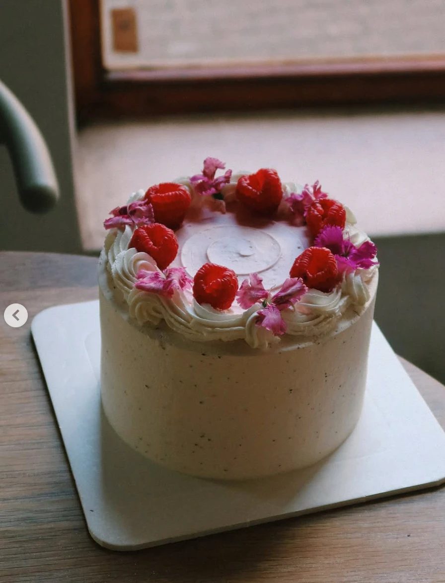 A vanilla buttercream layer cake topped with raspberries and edible flowers